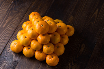 very close-up round bright beautiful delicious ripe tangerines stacked in a diamond on a brown wooden background