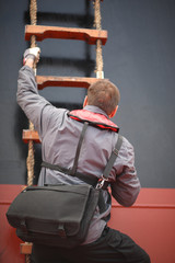 A man with a bag climbs the rope ladder to board the vessel standing in the roads