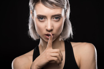 portrait of woman in bodysuit showing silence sign on black