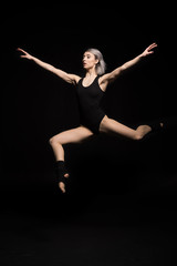 side view of focused jumping woman in bodysuit on black