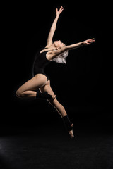 Obraz na płótnie Canvas side view of dancing woman in bodysuit on black