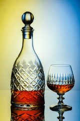 Crystal decanter and glasses with rum, carafe with whiskey on a glass table, colorful background