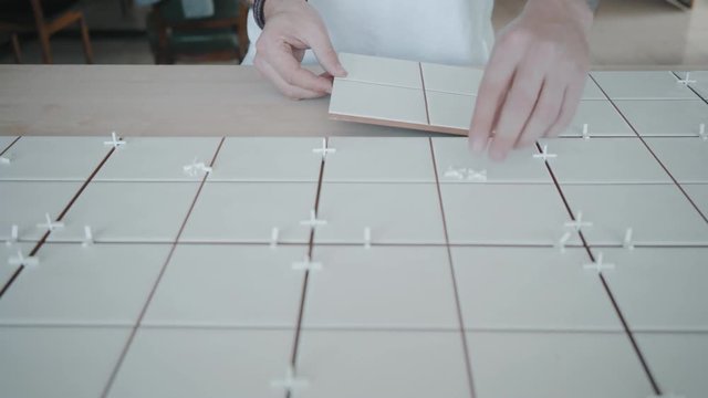 Front view, man uses plastic tile spacers to apply ceramic tile next to others and making new kitchen table in his house