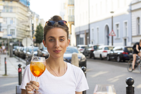Portrait of young woman toasting with aperitive at pavement cafe