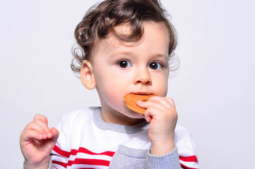 Portrait of a cute baby eating a biscuit. One year old kid eating biscuits by himself. Adorable curly hair boy being hungry. - 138076243