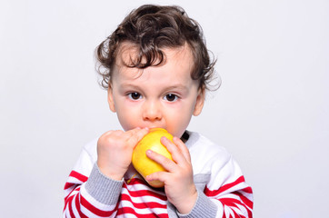 Fototapeta na wymiar Portrait of a cute baby eating an apple. One year old kid eating fruits by himself. Adorable curly hair boy being hungry biting on a big red apple.