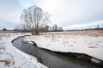 River between ice and snow covered fields. Yellowish fields with snow.