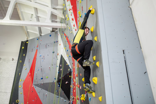 man climbing on practical wall indoor, with belay carabiners and rope