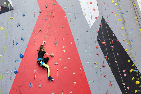 Concentrated sports woman climbing up the wall at indoor gym