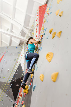 Fit sporty woman looking up at rock climbing wall at the gym and training