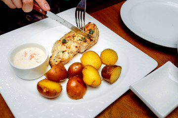 fork and knife in hand cut steak chicken breasts on a plate with potatoes in their skins