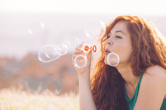 red hair woman blowing colorful bubbles outdoors.