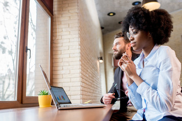 Beautiful african businesswoman and caucasian man working together with laptops near the window at...
