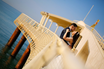 Groom and bride posing on a bridge near the sea