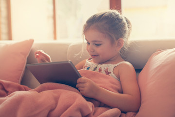 Young girl using a tablet sitting on the couch.