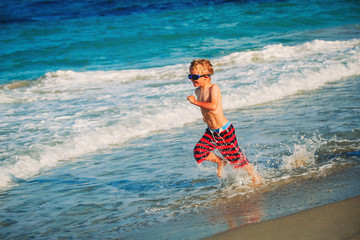 happy little boy run play with waves on beach
