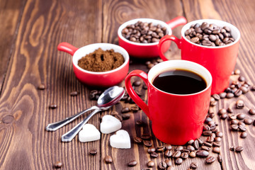 Two cups with coffee Cup with coffee beans Wooden background Coffee beans around red cups