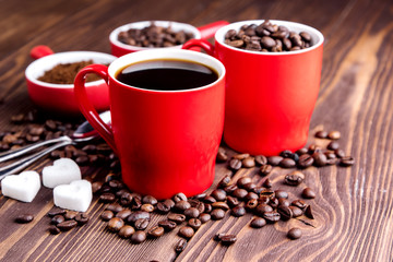 Two cups with coffee Cup with coffee beans Wooden background Coffee beans around red cups