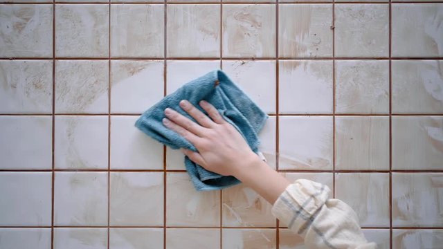 Girl hand wipes out with blue micro fiber cloth dried and dirty tile adhesive from custom made kitchen table with white glance ceramic, top view