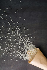 White rice scattered over the dark wooden table of a paper bag. View from above. Space for text.