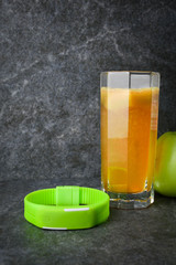 fitness bracelet glass with natural juice and apples on a stone against a dark background