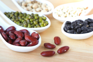 Assortment of beans and lentils in white spoon on wooden background. mung bean, groundnut, soybean, red kidney bean , black bean ,red bean and brown pinto beans . Healthy protein food.
