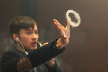 Young handsome white guy let rings out of steam. Vaping.