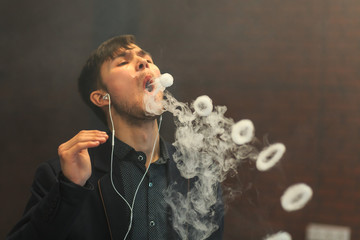 Young handsome white guy let rings out of steam. Vaping.