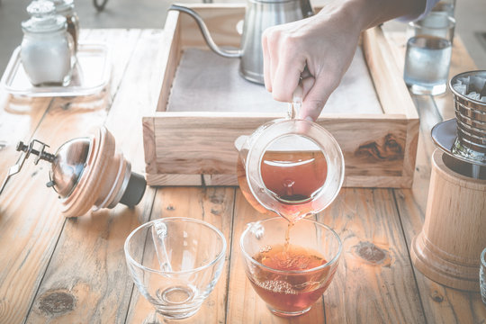 Barista pouring drip coffee in a glass cup with drip coffee set on the background.