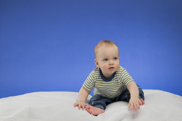 Fototapeta premium Funny little baby boy, sitting on the white blanket, studio shot, isolated on blue background