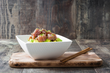 Hawaiian tuna poke bowl with avocado, radishes and sesame seeds on wooden background
