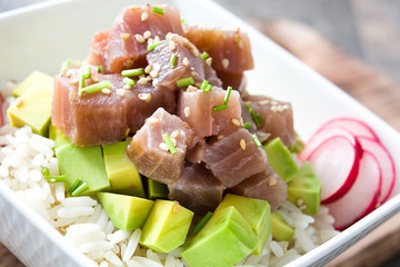 Hawaiian tuna poke bowl with avocado, radishes and sesame seeds on wooden background
