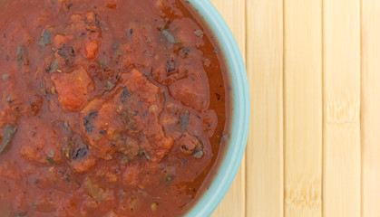 Top close view of fire roasted crushed tomatoes in a bowl atop a wood place mat.