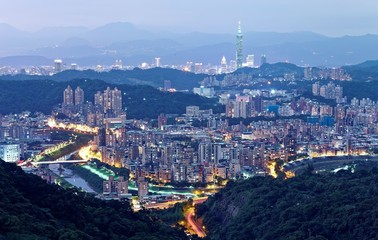 Fototapeta premium Aerial panorama of overpopulated suburban communities in Taipei at dusk, with Taipei 101 Tower in downtown, bridges over Xindian River & distant mountain silhouettes ~ Romantic Taipei in blue twilight