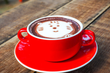 Hot cocoa and face cat  milk foam in the red cup on wood background