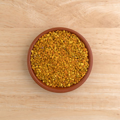 Top view of a small bowl of bee pollen granules on a wood table.