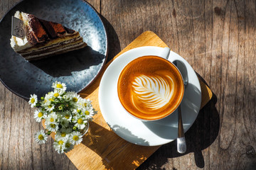 Coffee cup on a wooden table and the little flowers with cake.