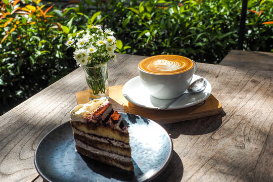Coffee cup on a wooden table and the little flowers with cake.