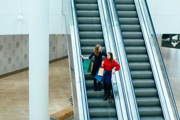 Top view of two elegant ladies to going down on the escalator.