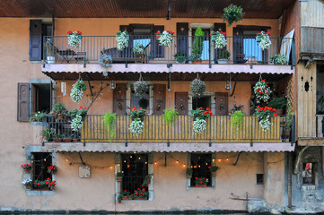 Wall of old house with shuttered windows and balconies decored colorful flowers in flowerpots