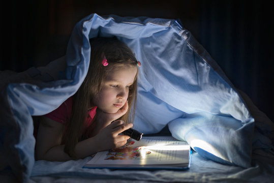 girl reading with a flashlight under the covers