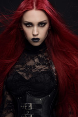 Young woman with red hair in black gothic costume on dark background