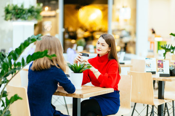  Fashion  young women with coffee cups sitting at table and talking in mall or cafe.