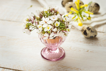 Spring delicate white yellow flowers in crystal egg cup, quail eggs, wood background, Easter decoration, soft colors
