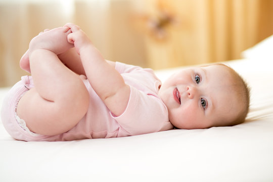 Funny smiling baby infant girl playing with her feet