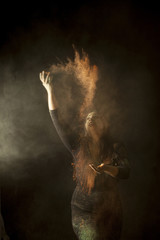 Indian woman dancing and throwimg colored dust in the air isolated on black background