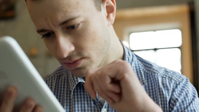 Thoughtful man sitting in the cafe and browsing internet on tablet
