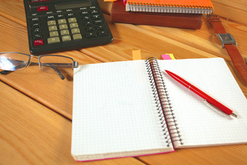 surface of a wooden table with notebook, smartphone, eye glasses, and pen
