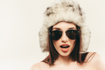 Beautiful and happy young woman isolated on white and wearing a fur hat and sunglasses
