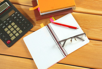 surface of a wooden table with notebook, smartphone, eye glasses, and pen